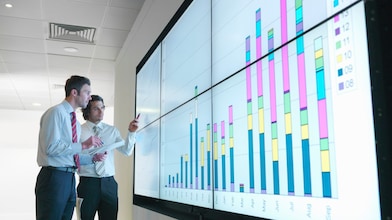 Business men analyse reports displayed on a large digital screen