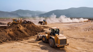 Two bulldozers and a backhoe loader removing waste rock on a mining site