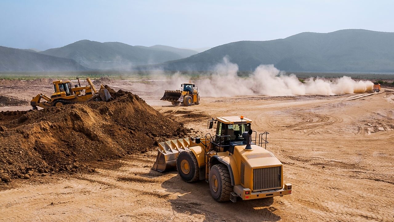 Two bulldozers and a backhoe loader removing waste rock on a mining site