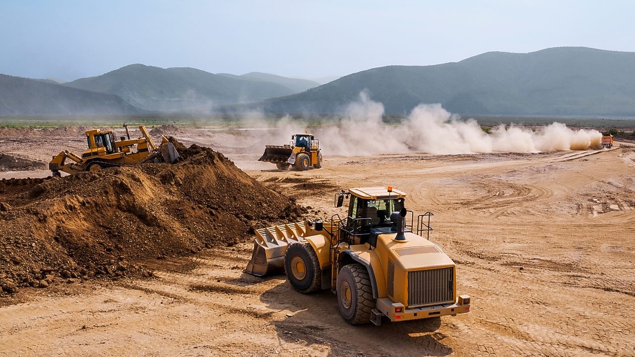 Two bulldozers and a backhoe loader removing waste rock on a mining site