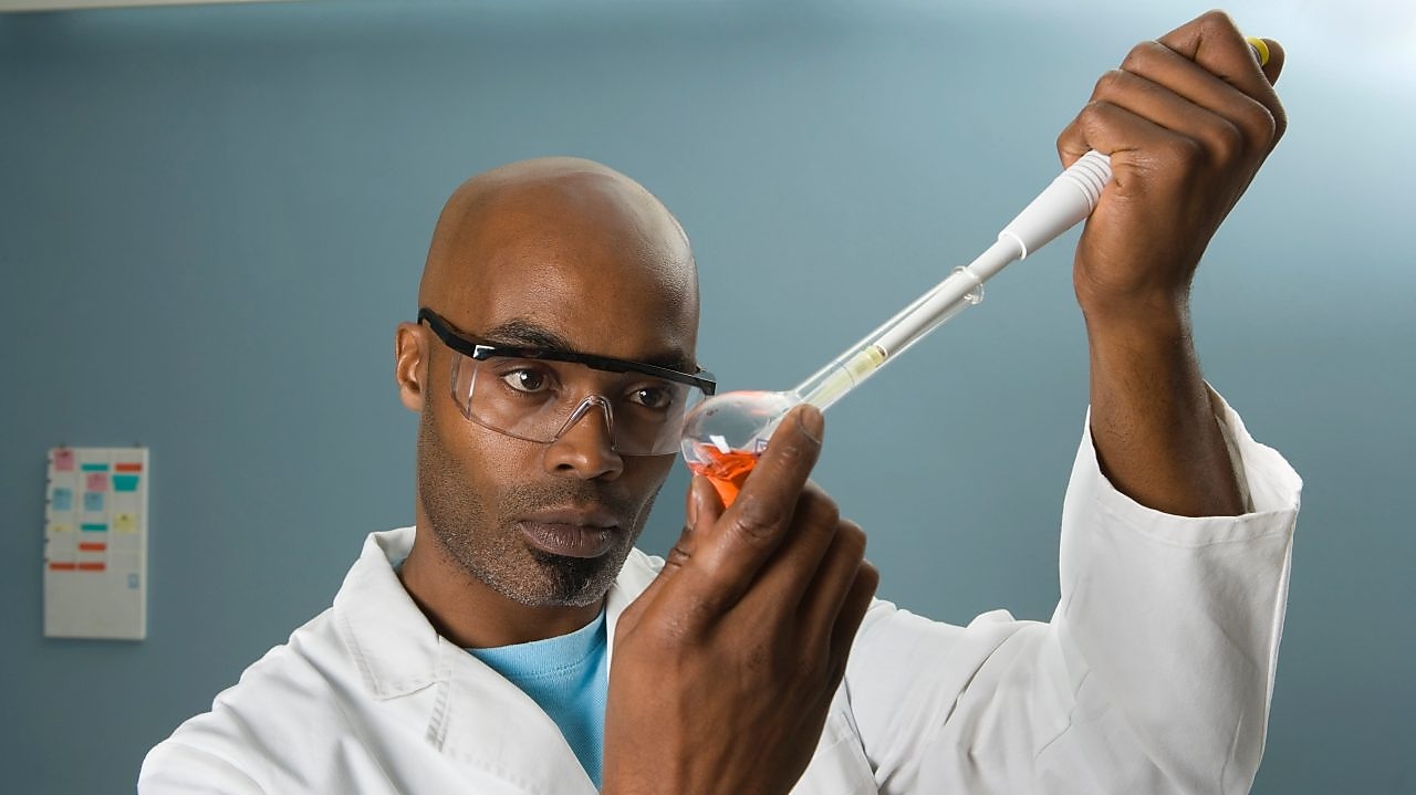 Male laboratory technician holding a flask and pipette testing diesel
