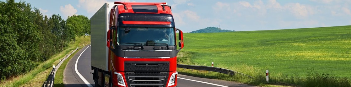 Red truck driving on asphalt road in a rural landscape