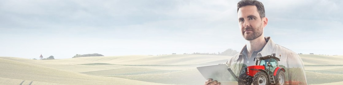 Man reading a document with a background of fields and a red tractor