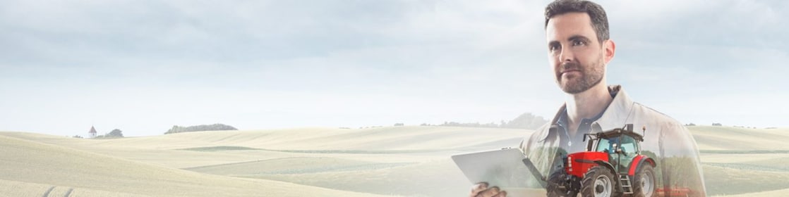 Man reading a document with a background of fields and a red tractor