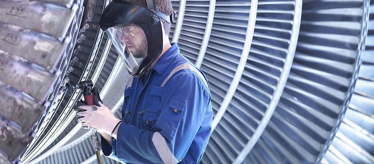 Engineer repairing steam turbine blade with grinder in workshop