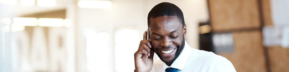A person in front of a laptop setting while talking on a mobile phone.