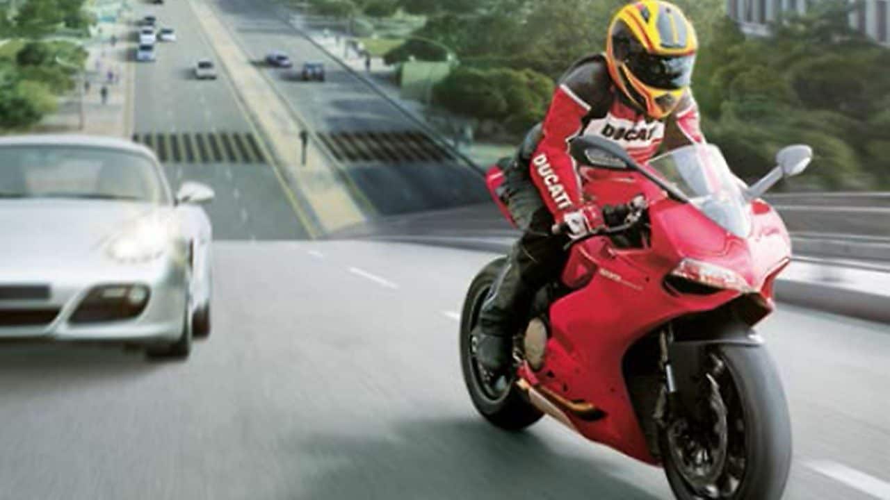 Red motorcycle and rider on a road with cars and buildings in the background