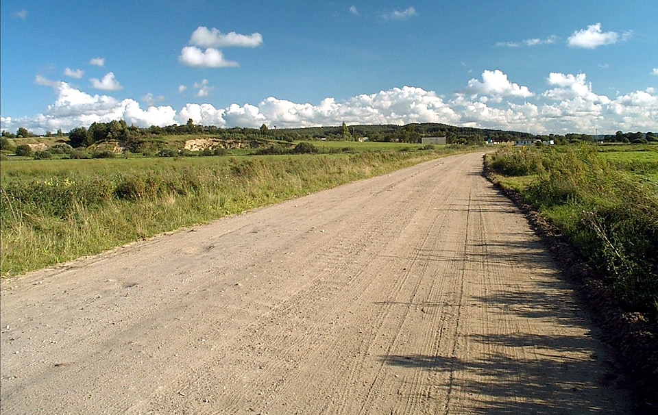 Looking down a long dirt road surrounded in green countryside